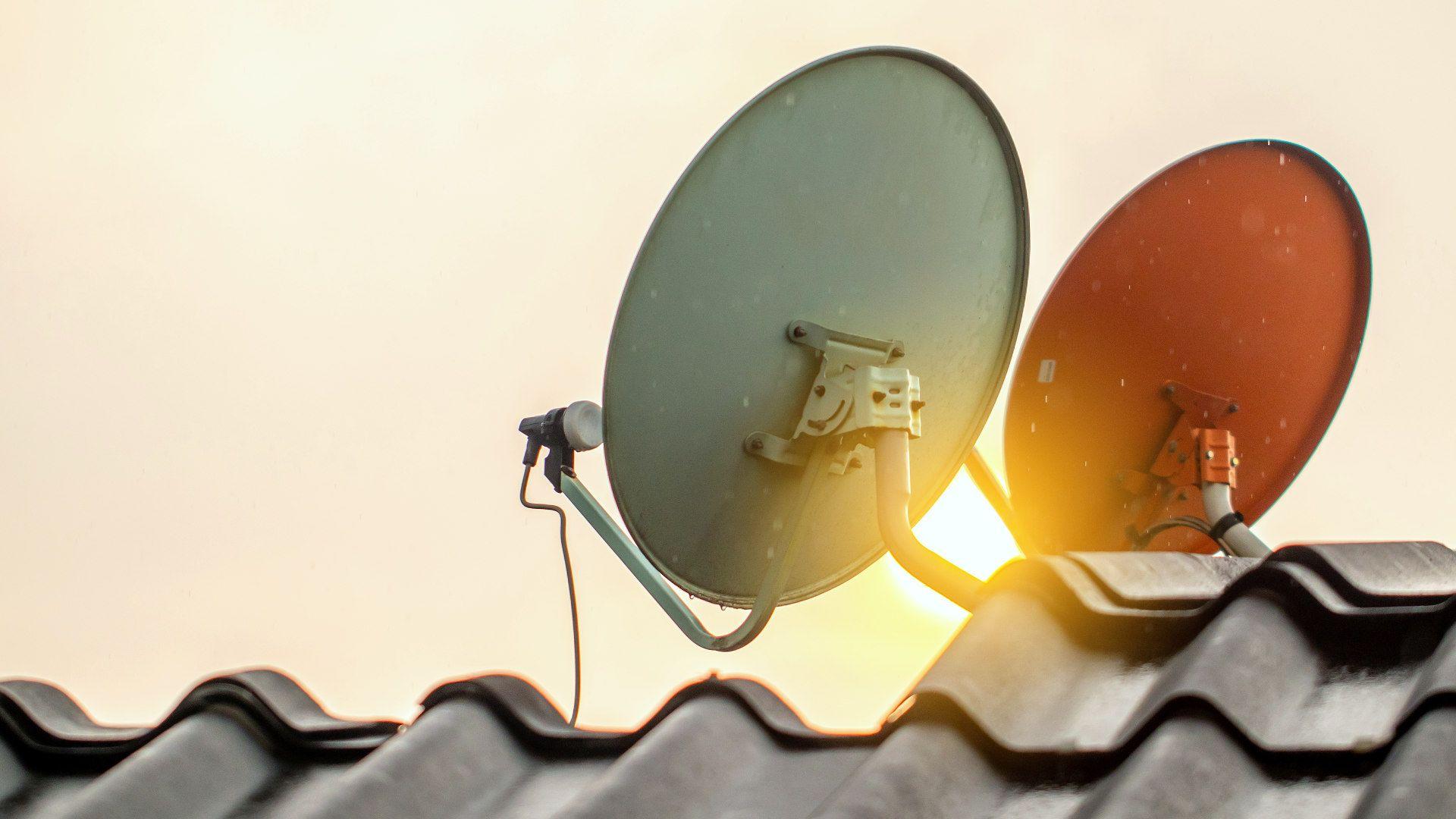 Zwei Parabolantennen (Satellitenschüsseln) sind auf einem Ziegeldach montiert und richten sich gegen den Himmel.