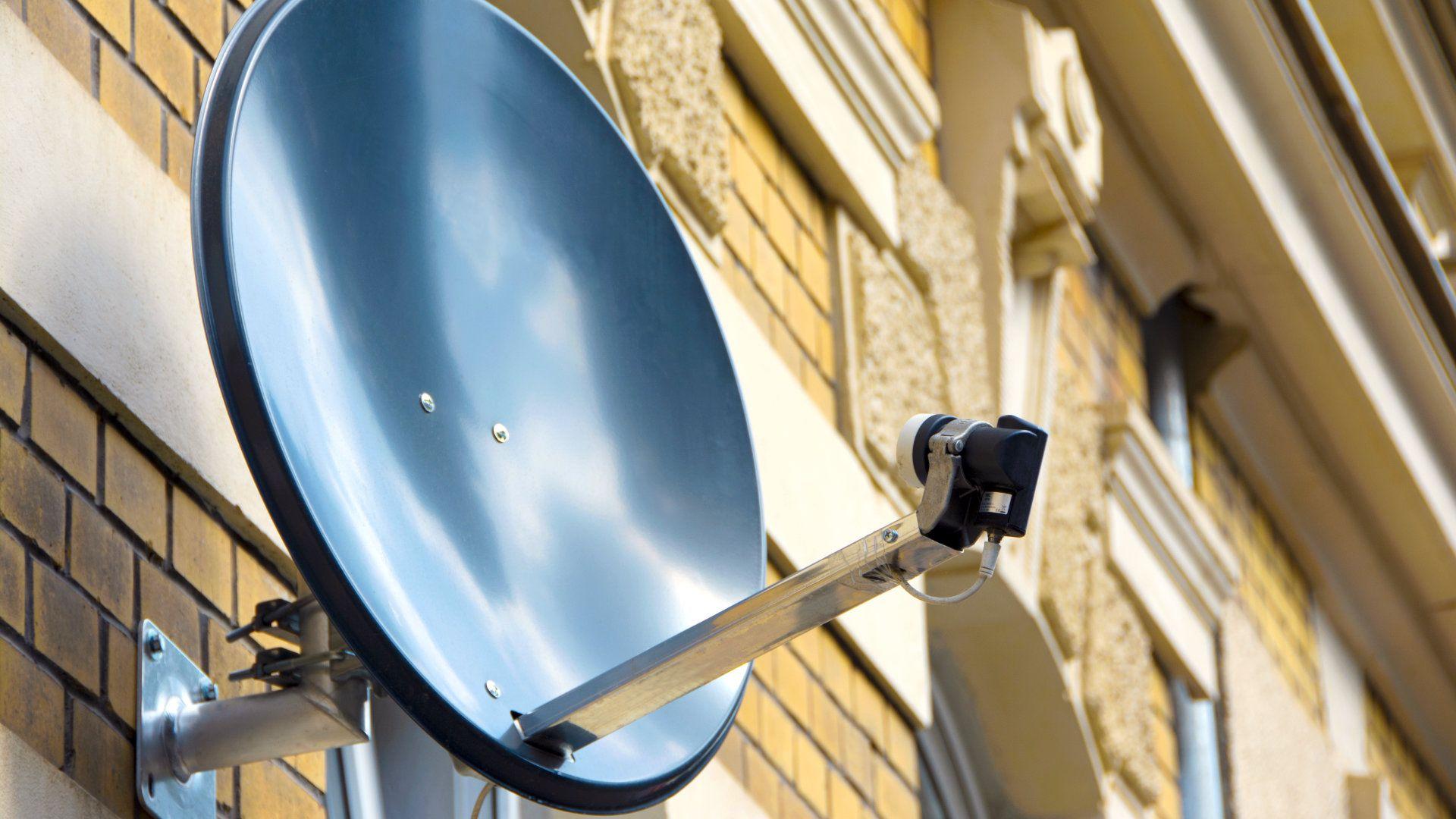 Eine Satellitenschüssel, die mit einem speziellen Wandhalter an einer Hauswand montiert wurde. 